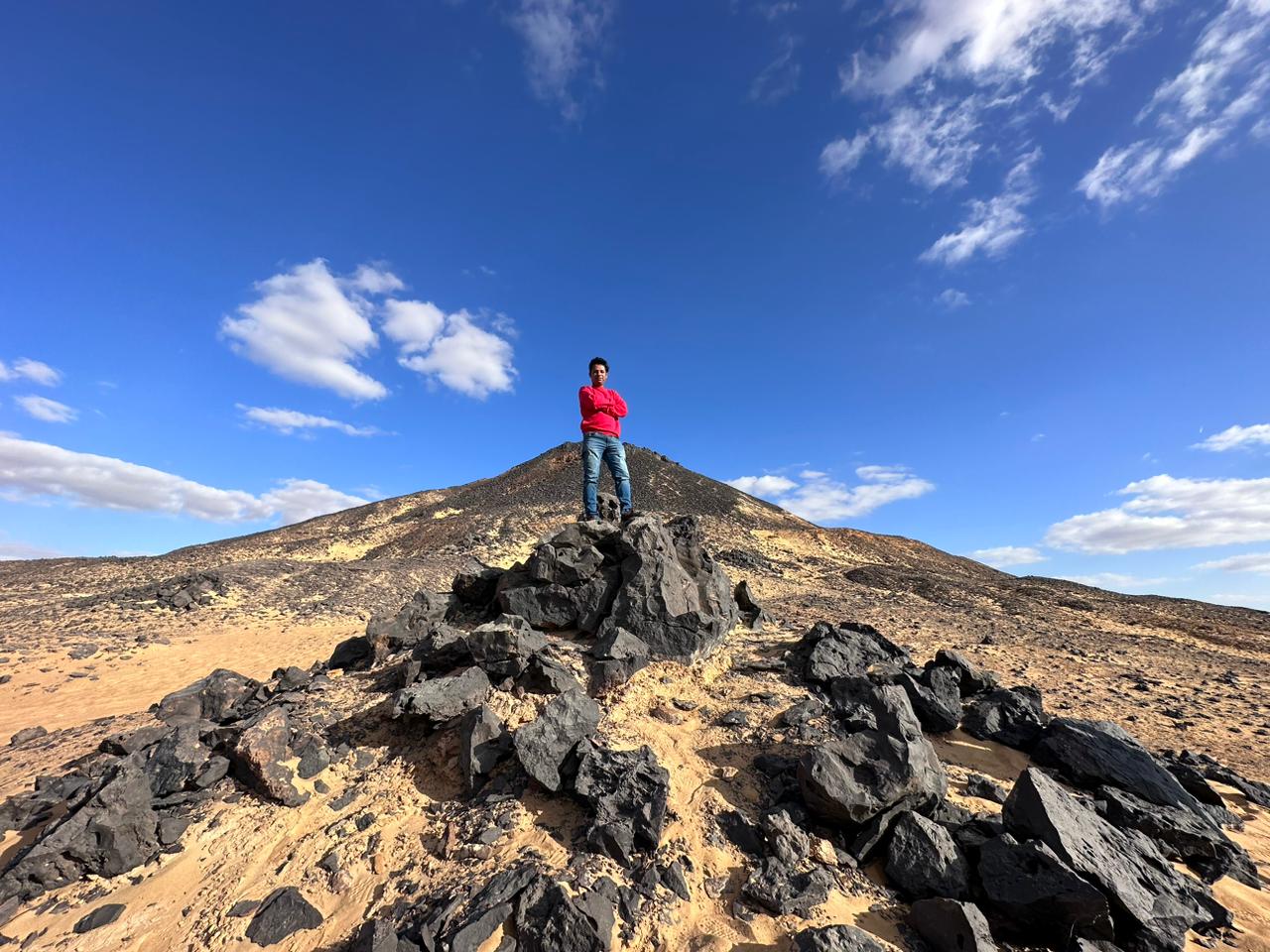 A lone traveller standing on a rocky summit beneath a wide blue sky